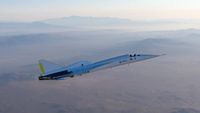 a needle-nosed white and silver plane flies over a desert-mountain landscape