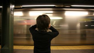 A young boy covers his ear as a subway train screeches by