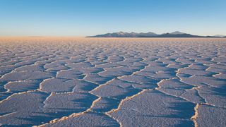 The salt crust at Salar de Uyuni bathed in orange light with mountains in the background.